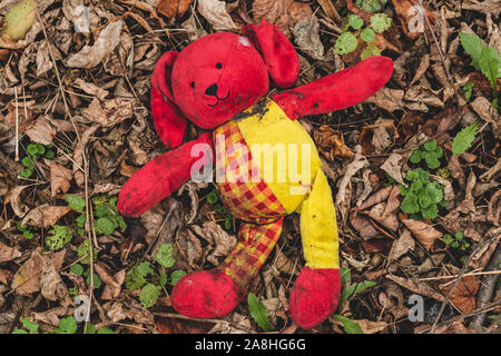 Plüsch Spielzeug Hund wälzen sie sich in Laub. Verloren schmutzig rot Spielzeug auf dem Boden liegt im Park. Stockfoto