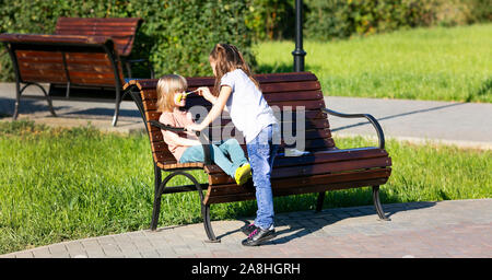 Ein kleines Mädchen ist die Anwendung aqua Make-up von 5 Jahre alten Jungen, sitzen auf einer Bank in einem Park ist. Stockfoto