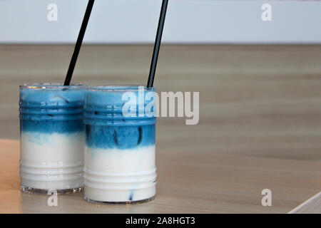 Zwei Gläser iced Erbse latte. Blue Tee 2-in-1-Cocktail mit Milch auf Holztisch mit schwarz Stroh und Eis. Kopieren Sie Platz für Text. Alkoholfreie und sof Stockfoto