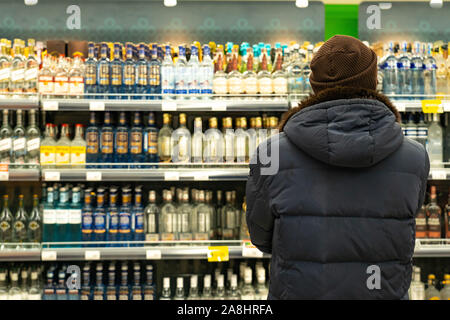 Ein Mann vor der Zeilen von Alkohol auf dem Markt. Der Käufer wählt das Produkt Stockfoto