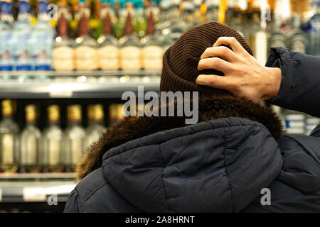 Ein Mann vor der Zeilen von Alkohol auf dem Markt. Der Käufer wählt das Produkt Stockfoto