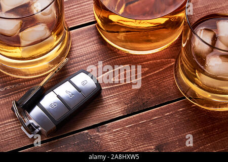 Moderne Autoschlüssel auf hölzernen Tischplatte in bar an. Glas und Flasche Whiskey oder andere Alkohol mit Eis. Passend für die Artikel auf Trunkenheit am Steuer. Stockfoto