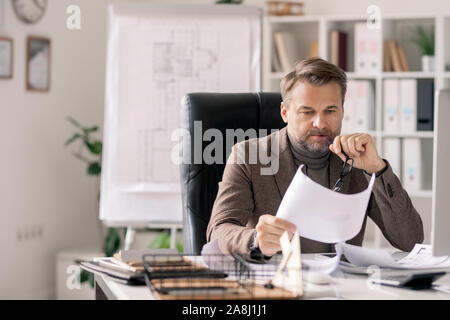 Nachdenklich reife Architekt auf Skizze auf Papier im Sessel sitzt Stockfoto