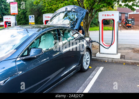 Ein Mann gegen sein Auto an der Tesla Ladestation an der Autobahn services in Großbritannien, elektrische Ladung Stockfoto