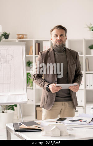 Zuversichtlich reife Architekt in formale mit Tablette, während man vom Schreibtisch aus Stockfoto
