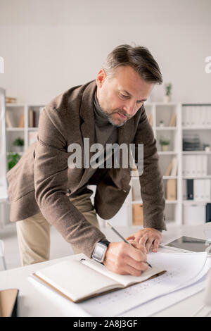 Reifen Architekt Bücken öffnen Notebook auf dem Schreibtisch während der Arbeit Notizen Stockfoto