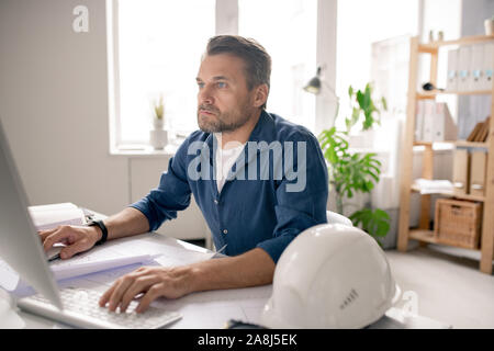 Ernst Ingenieur konzentriert sich auf Arbeiten, während Sitzen vor dem PC-Bildschirm Stockfoto