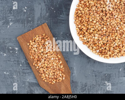 Buchweizengrütze in Weiß und Braun Holzspachtel auf einem dunklen konkreten Hintergrund mit kopieren. Gesunde Ernährung Konzept Stockfoto