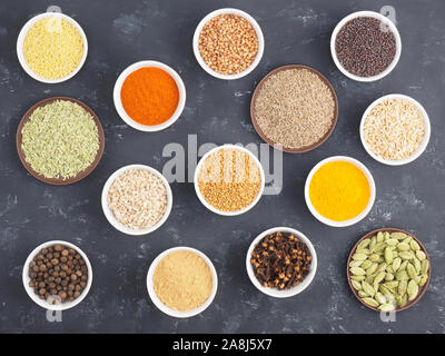 Buchweizen, Hirse, Piment, Fenchel, Hafer, Pfeffer, Chili, Masala, Nelken, Bockshornklee, Kurkuma, Kreuzkümmel, Senfkörner, Grüner Kardamom auf schwarzem Beton ba Stockfoto