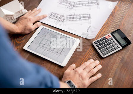 Der moderne Ingenieur lehnte sich auf hölzernen Tisch während die Biegung über Tablet Stockfoto