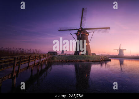 Kinderdijk traditionellen Windmühlen in den Niederlanden. Kalt und eisig Sonnenaufgang. Reflexionen über das Eis des zugefrorenen Kanal. Glow Atmosphäre. Brücke. Winter Stockfoto