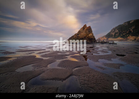 Dreieckige Felsformation und Muster Reflexionen auf dem Sand, in einer Strand von Asturien, kantabrische Küste, in Spanien. Playon de Bayas. Bewölkt morgen. Stockfoto