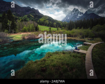 Person im Deck, in der Nähe des Sees in Zelenci Federn, Slowenien. Türkis-blauen See in der Nähe der Bergen. Bewölkten Tag. Stockfoto