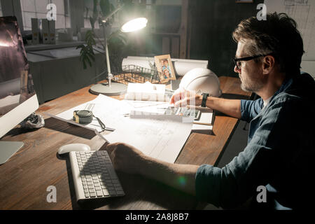 Moderne Techniker arbeiten mit Skizzen, während im Büro spät Stockfoto