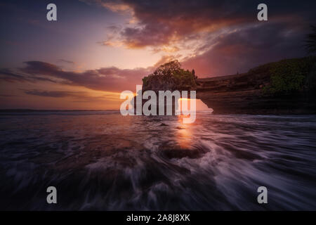 Pura Batu Bolong, ein Hindu Tempel über eine Klippe Arch, im Süden Bali, Indonesien. Bewölkt, Sonnenuntergang und die Wellen in den nahe gelegenen Strand. Stockfoto