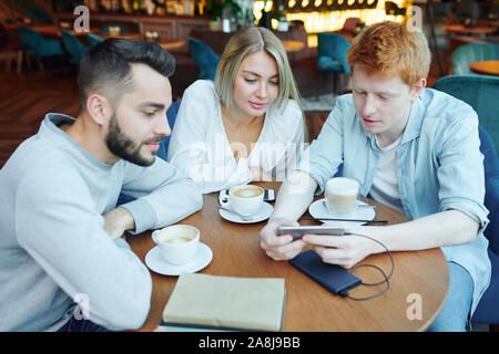 Gruppe von college Freunde Kaffee und beobachtete neugierig Material in Smartphone Stockfoto