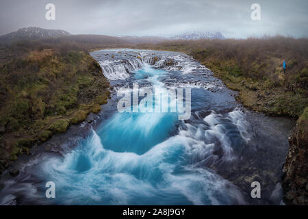 Brúarfoss, einer schönen Türkis Wasserfall in Island. Herbst bewölkten Tag, Gras. Bekannte touristische Destination. glazialen reines Wasser. Stockfoto