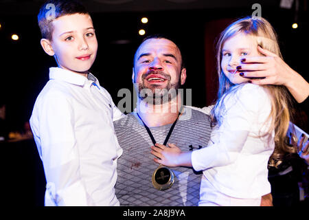 Gerne Vater mit blutigen Nase und Lippe trägt stolz, Sohn und Tochter auf seine Hände nach dem Gewinn amature Kampf in White Collar Boxing League in Kiew Stockfoto