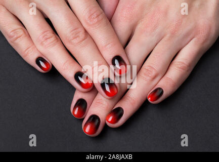 Zwei weibliche Hände mit Rot Schwarz ombre gradient Nägel auf dunklem Hintergrund Stockfoto