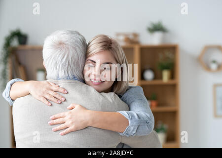 Liebevolle Frau mit toothy Lächeln und geschlossenen Augen ihr älterer Vater umarmt Stockfoto