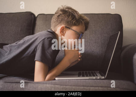 Junge Schüler Hausaufgaben liegen auf einem mit Laptop Sofa. Kaukasische boy Video online ansehen zu Hause. Jugendlich Freizeit mit dem Computer. Stockfoto