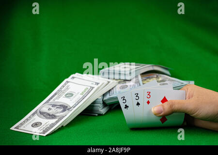 Poker Casino Glücksspiel und das Geld stack von 100 US-Dollar Banknoten am grünen Hintergrund, Hand, die Karte Nummer 3 Karten Stockfoto