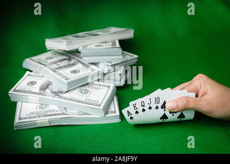 Poker Casino Royal Straight Flush und das Geld stack von 100 US-Dollar Banknoten am grünen Hintergrund, Hand, die Spielkarte Pik 5. Stockfoto