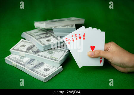 Poker Casino Royal Straight Flush und das Geld stack von 100 US-Dollar Banknoten am grünen Hintergrund, Hand, die Spielkarte Herz 5. Stockfoto