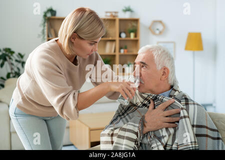 Junge Frau, die ihren kranken Vater Glas Wasser geben, während die Pflege von ihm Stockfoto