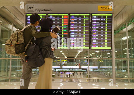 Junges Paar mit Reisepass in Händen an blurry Flight Information Display am Flughafen suchen Stockfoto