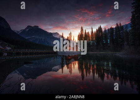 Sonnenaufgang am Emerald Lake, ein Juwel in den Rockies. Spiegelbild, bunte Wolken, eine Kabine und die Bäume. Kleines Haus am Ende der Brücke. Yoho. Stockfoto