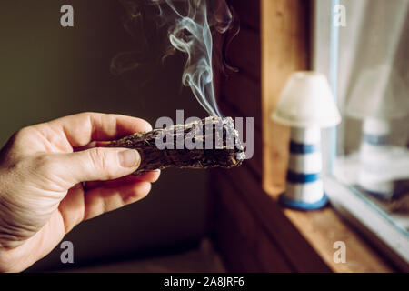 Frau hand Kraut Bündel getrockneter Salbei smudge Stick rauchen. Es wird geglaubt, negative Energie zu reinigen und Wohnräume in Zimmer reinigen Stockfoto