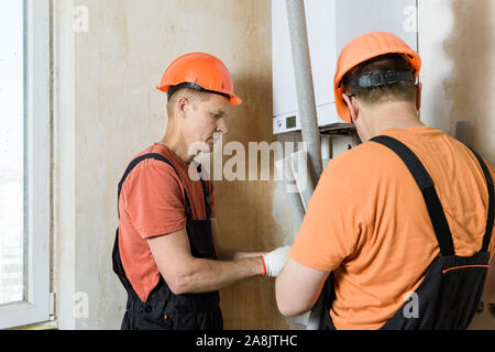 Arbeitnehmer sind die Installation von thermische Isolierung der Rohre mit einer Home Gas Boiler. Stockfoto