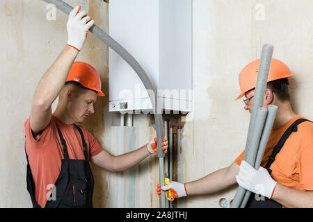Arbeitnehmer sind die Installation von thermische Isolierung der Rohre mit einer Home Gas Boiler. Stockfoto