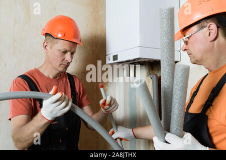 Arbeitnehmer sind die Installation von thermische Isolierung der Rohre mit einer Home Gas Boiler. Stockfoto