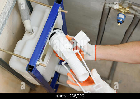 Ein Arbeitnehmer ist das Einfügen der Toilettenspülung Ventil in den eingebauten Tank. Ansicht von oben. Stockfoto