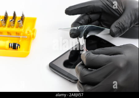Menschliche Hände entfernen eine Film aus dem Schutzglas auf dem Bildschirm eines Smartphones. Stockfoto