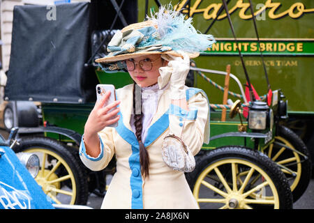 Junge Dame in Vintage viktorianische Kleidung mit gefiederten Hut auf Ihr Handy suchen, Anachronismus erstellen Stockfoto