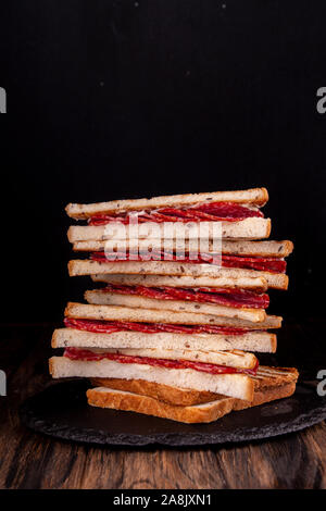 Heep von Sandwiches geröstetes Brot und Salami auf Schwarz. Fast food ungesunde Konzept Stockfoto