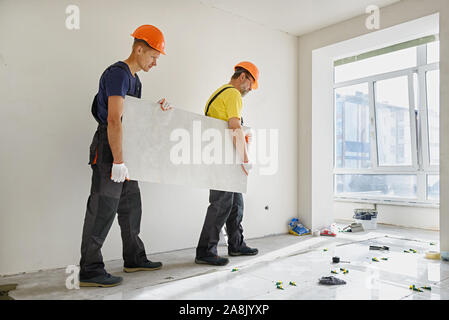 Arbeitnehmer sind mit einem großen Keramische Fliese für die Installation auf den Boden. Stockfoto