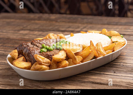 Rindersteak mit rustikalen Kartoffel- und ricei auf Holztisch, Hintergrund, weiches Licht Stockfoto