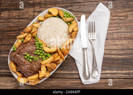 Rindersteak mit rustikalen Kartoffel- und ricei auf Holztisch, Hintergrund, weiches Licht Stockfoto