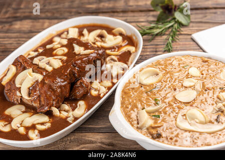Risotto mit Filet Mignon. Risoto und Rindfleisch mit Pilzen in einer weißen Platte auf einem weißen Hintergrund. Weiches Licht. Italienisches Essen. Stockfoto