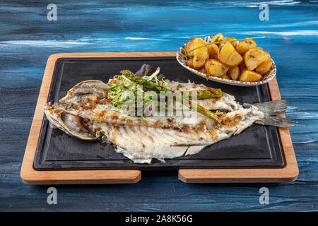 Den gegrillten Wolfsbarsch auf dem Holzbrett. Den gegrillten Wolfsbarsch, serviert auf einem Teller mit verschiedenen Saucen und mit Petersilie und Zitrone eingerichtet. Stockfoto