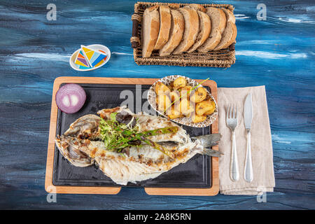 Den gegrillten Wolfsbarsch auf dem Holzbrett. Den gegrillten Wolfsbarsch, serviert auf einem Teller mit verschiedenen Saucen und mit Petersilie und Zitrone eingerichtet. Stockfoto