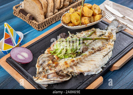 Den gegrillten Wolfsbarsch auf dem Holzbrett. Den gegrillten Wolfsbarsch, serviert auf einem Teller mit verschiedenen Saucen und mit Petersilie und Zitrone eingerichtet. Stockfoto