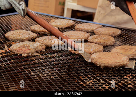 Eine Hand mit einem Spachtel spiegeln einen Burger Fleisch auf dem Grill Stockfoto