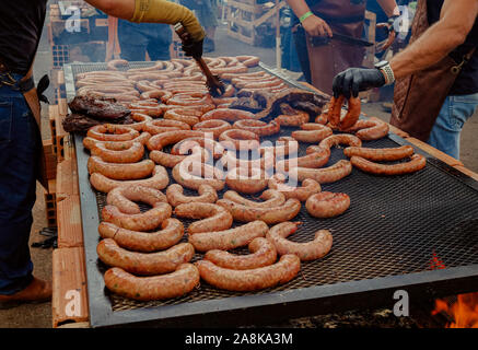 Zwei Hände Positionierung eine Menge Wurst in einem Grill in der Sonne Stockfoto