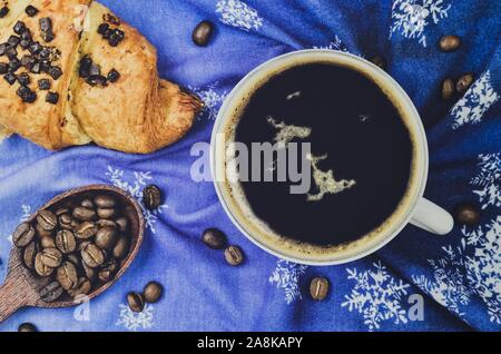 Interessante winter Konzept für Kaffee serviert. Schwarzer Kaffee mit Gipfeli auf einem blauen Hintergrund mit Schneeflocken. Stockfoto