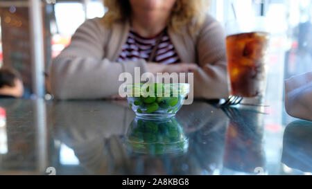 Eine Glasschale mit Schale versehenen Edamame Sojabohnen auf ein Restaurant Table Top vor der Frau. Stockfoto